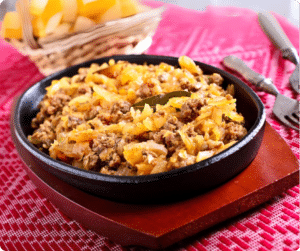 EIne Pfanne mit Gericht aus geschmortem Kraut, Faschiertem und Zwiebeln auf einem Tisch.