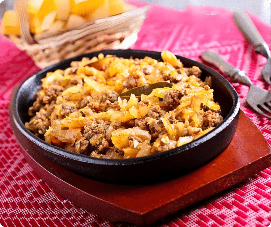 EIne Pfanne mit Gericht aus geschmortem Kraut, Faschiertem und Zwiebeln auf einem Tisch.