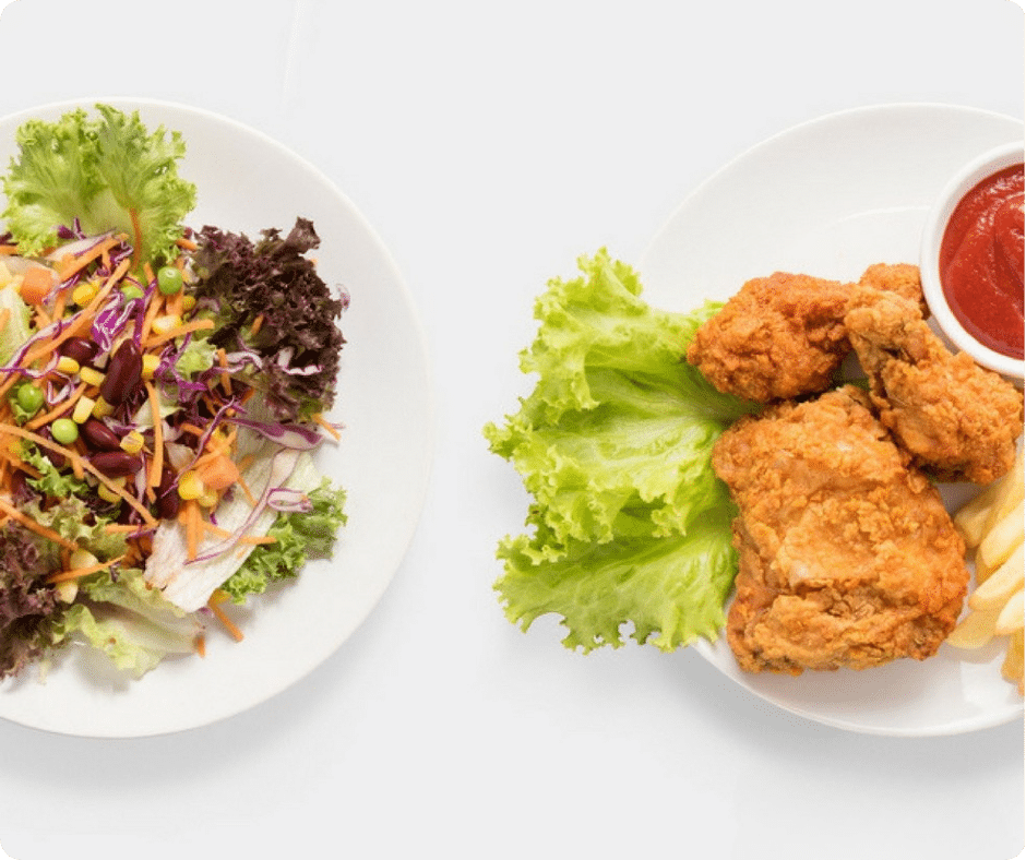 2 Teller - einer mit gesundem Salat, einer mit Schnitzel - auf einem weißen Tisch