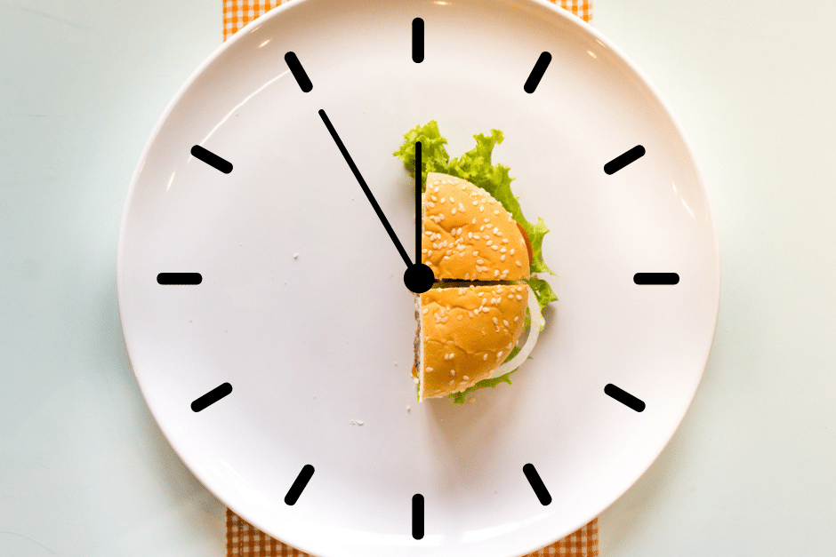 Ein weißer Teller mit nur einem halben Burger - darüber sieht man grafisch das Ziffernblatt einer Uhr