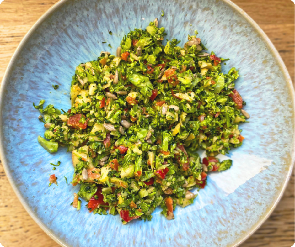 Blauer Teller mit Salat aus fein gehacktem Brokkoli, Apfel und Paprika auf einem Holztisch