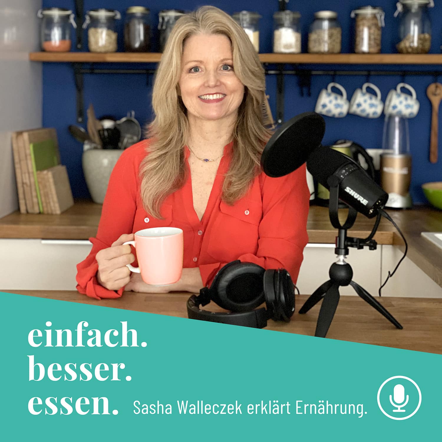 Sasha Walleczek sitzt in einer Küche mit einer Tasse Tee in der Hand. Vor ihr sieht man ein Mikrofon und Kopfhörer.