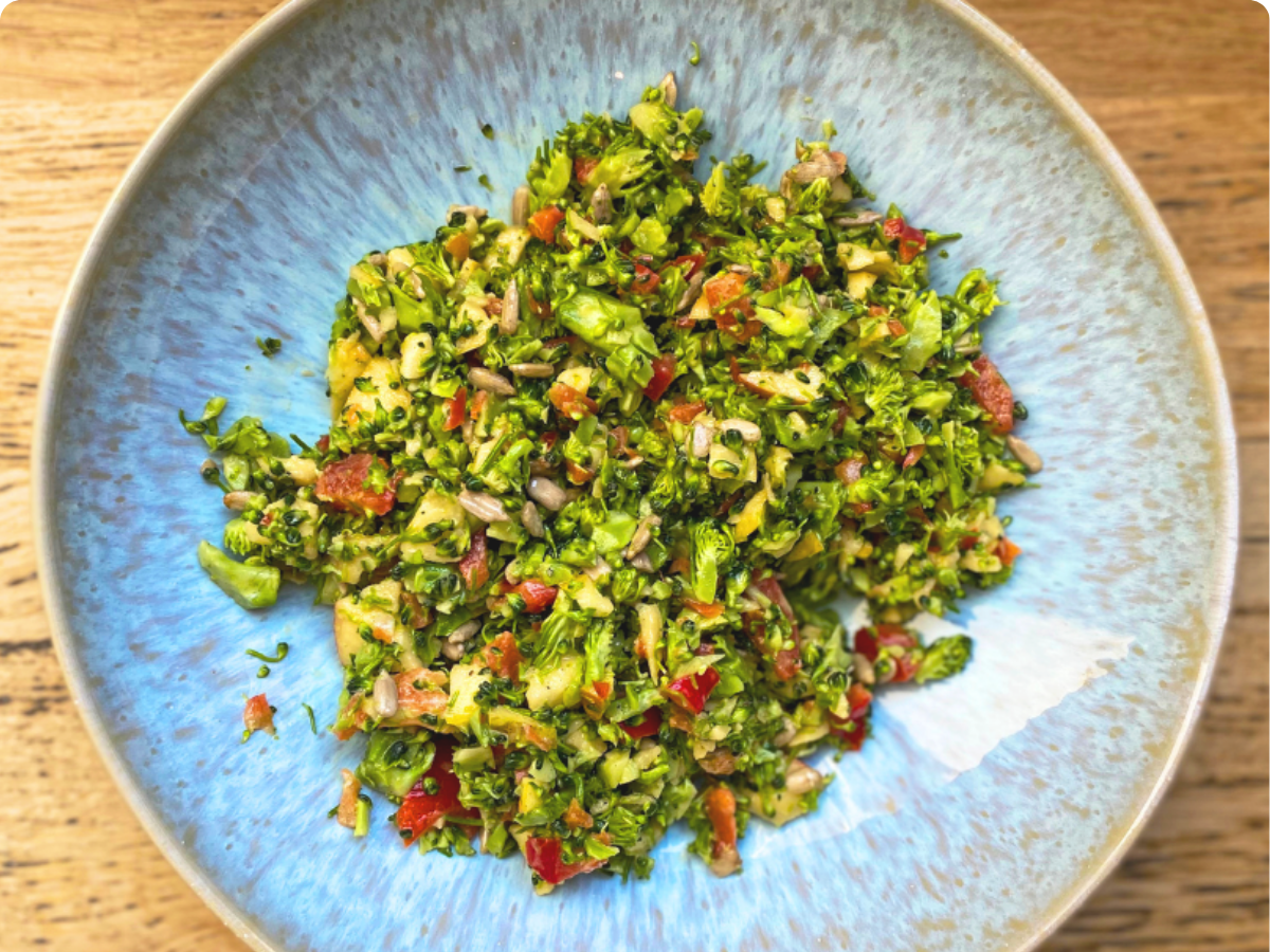 Blauer Teller mit Salat aus fein gehacktem Brokkoli, Apfel und Paprika auf einem Holztisch