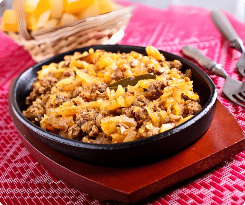 EIne Pfanne mit Gericht aus geschmortem Kraut, Faschiertem und Zwiebeln auf einem Tisch.